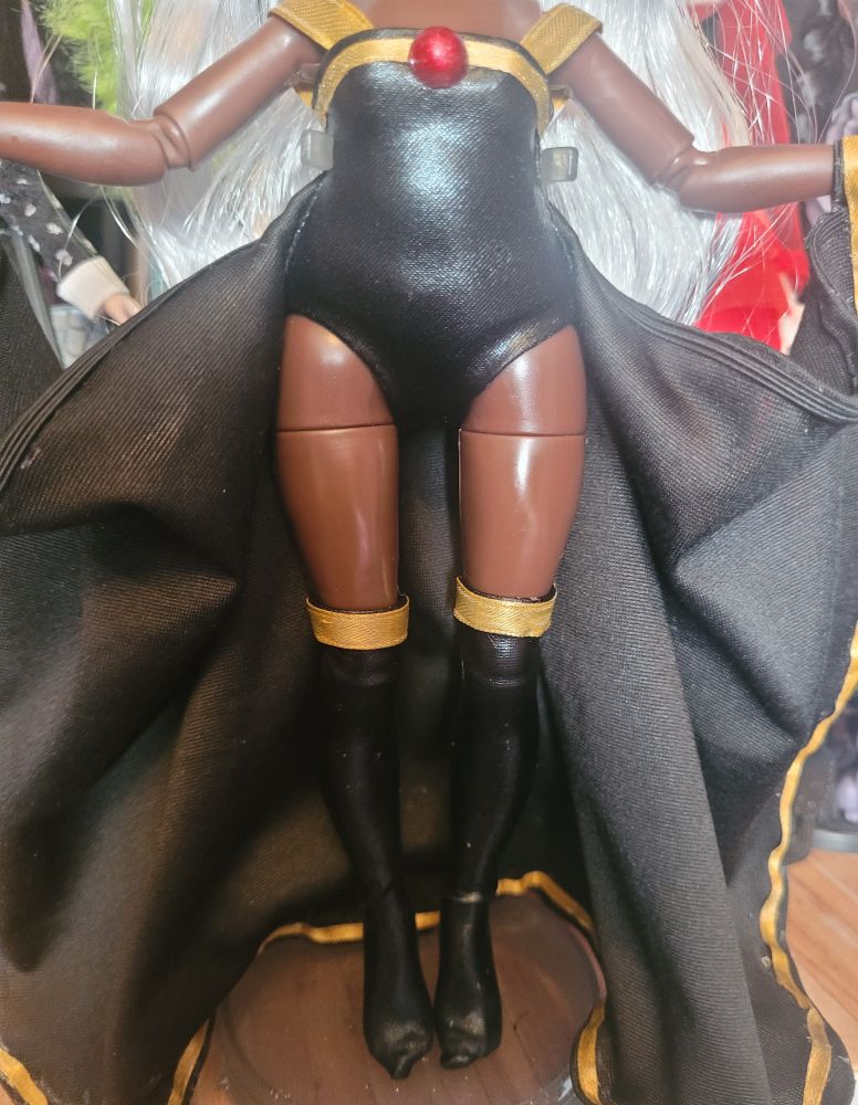 Rainbow high Ayesha Sterling Doll turned into Custom X-Men Storm. Wearing a black leotard with black thigh highs and cape, trimmed with gold ribbon. Image cut off at neck.