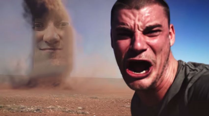 the "tornado selfie" meme (a man yelling into the camera with a tall sand funnel approaching behind him) but the storm has the exaggerated face made by Ed Zitron, aka The Smiling Man, photoshopped into it