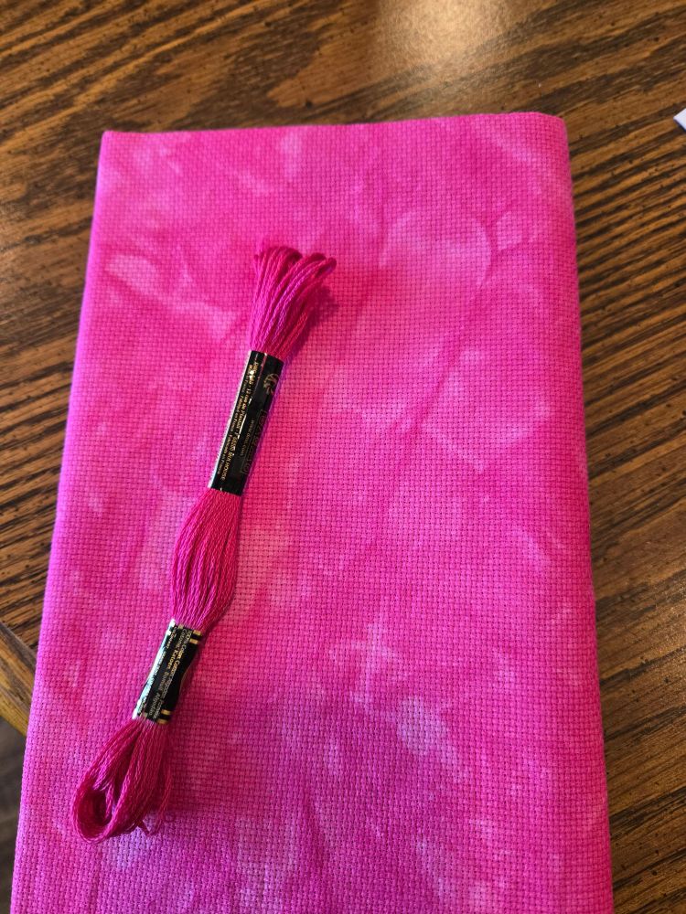DMC thread number 3804 is laying on Aida cross stitch fabric tie-dyed Barbie pink