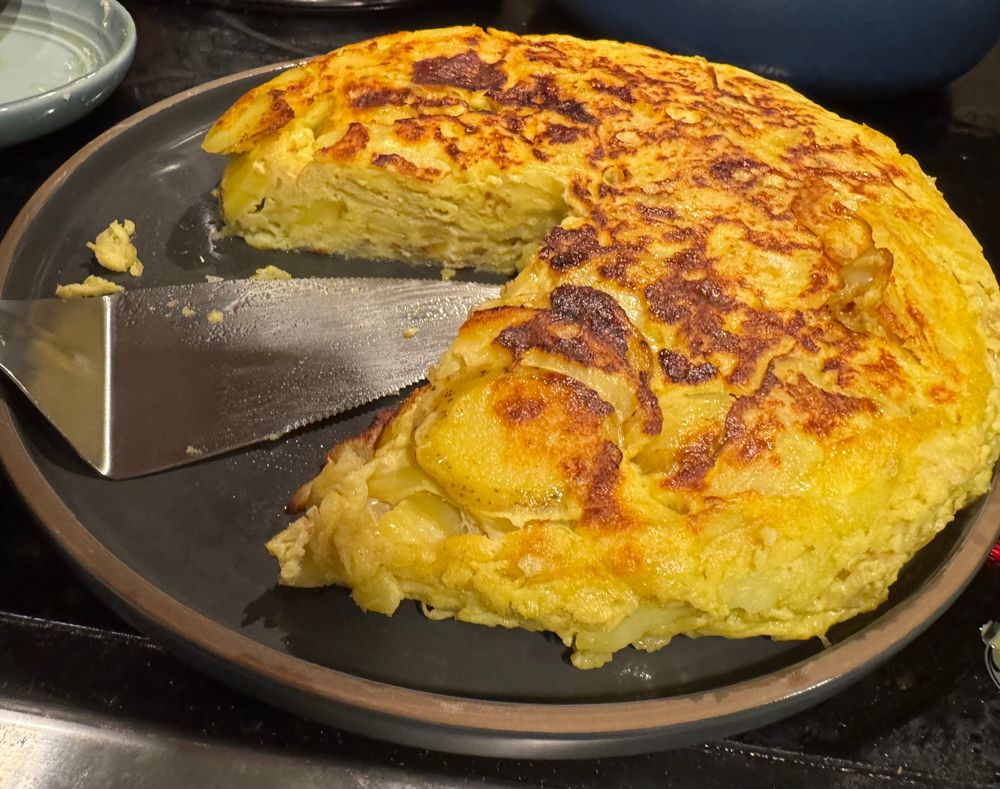 photo of a tortilla española with a slice removed. the cake slicer is visible, as is a dirty spoonrest and stovetop, because i was VERY HUNGRY and just wanted to eat the damn thing. i'll work on my food photography next time okay?????