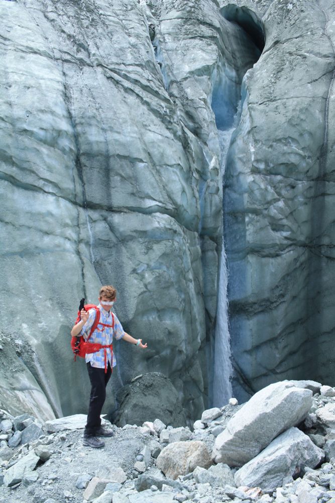 Man in flowery shirt stands in front of a glacial waterfall in Switzerland 