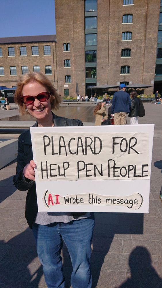 Author holding sign that reads "Placard for help pen people (AI wrote this message" 