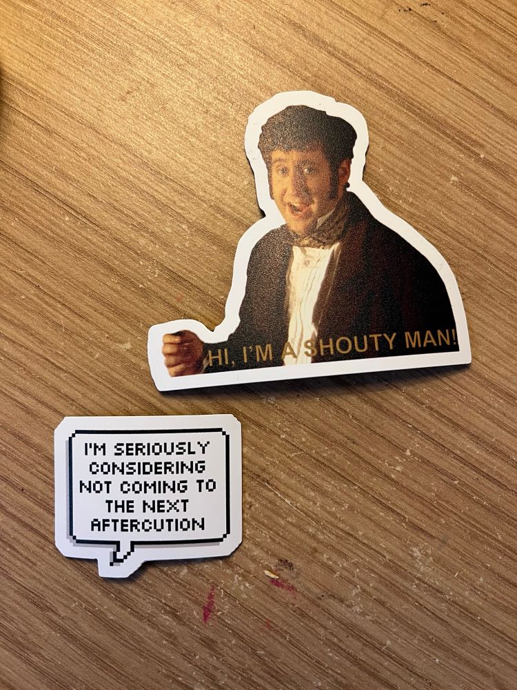 Two fridge magnets. One is of a man (the amazing Jim Howick) with the words HI, I’M A SHOUTY MAN printed on the bottom. The other is a speech bubble. The text inside says ‘I’m seriously considering not coming to the next aftercution’ 