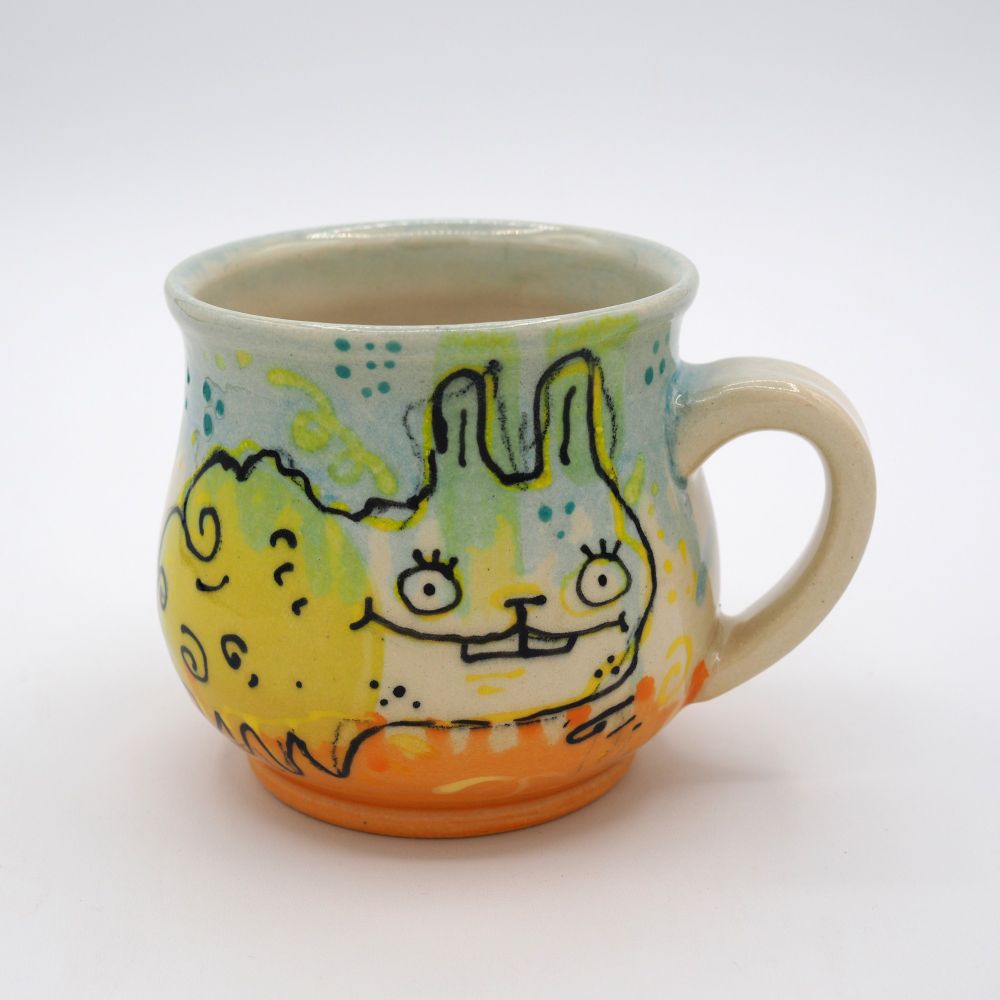 A strange doodle bunny over a blue and orange mug.