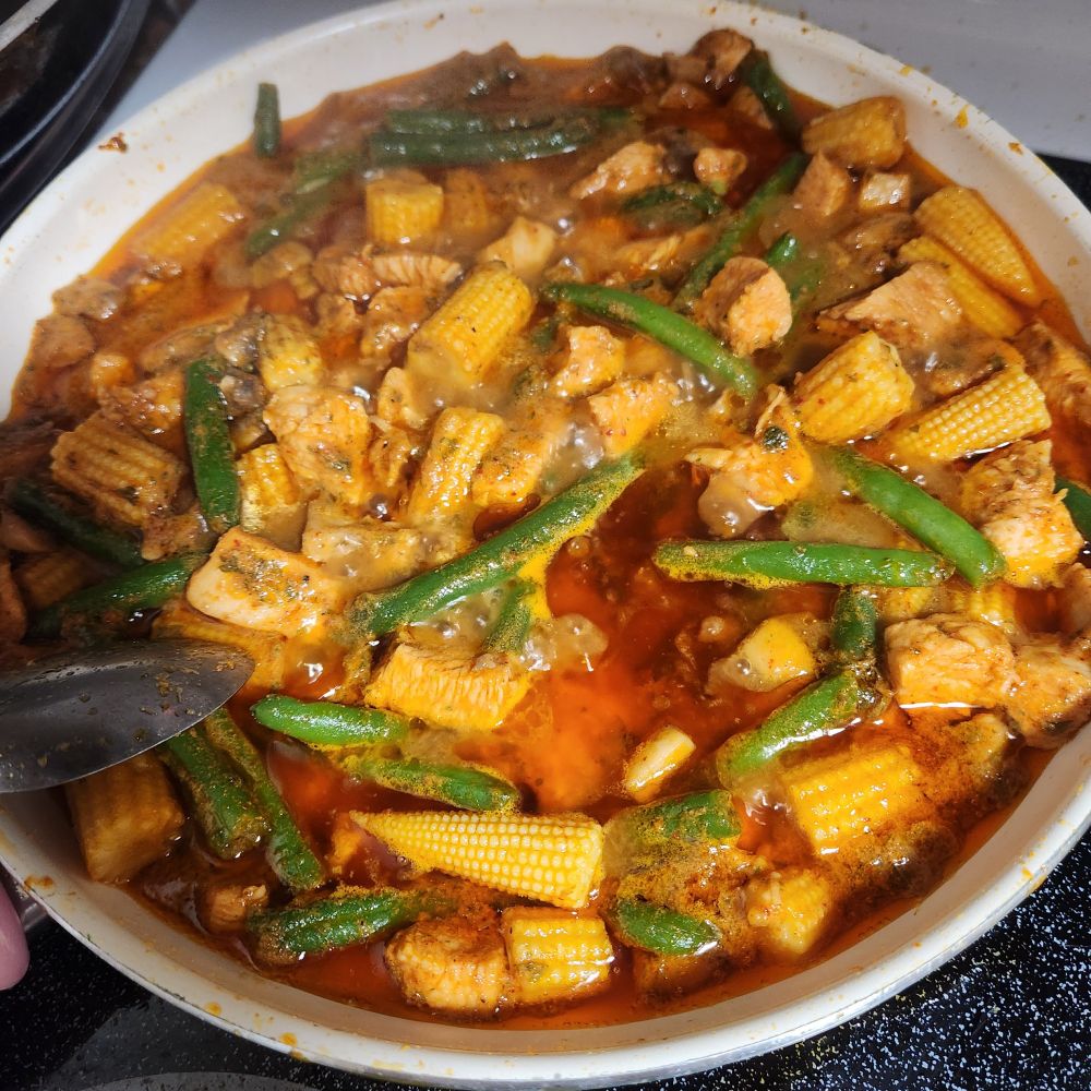 A photo of a pan cooking red curry with green beans, baby corn, mushrooms, and chicken with parsley sprinkled in.
