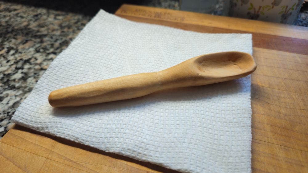 A hand-carved wooden spoon sits freshly oiled on a paper towel.