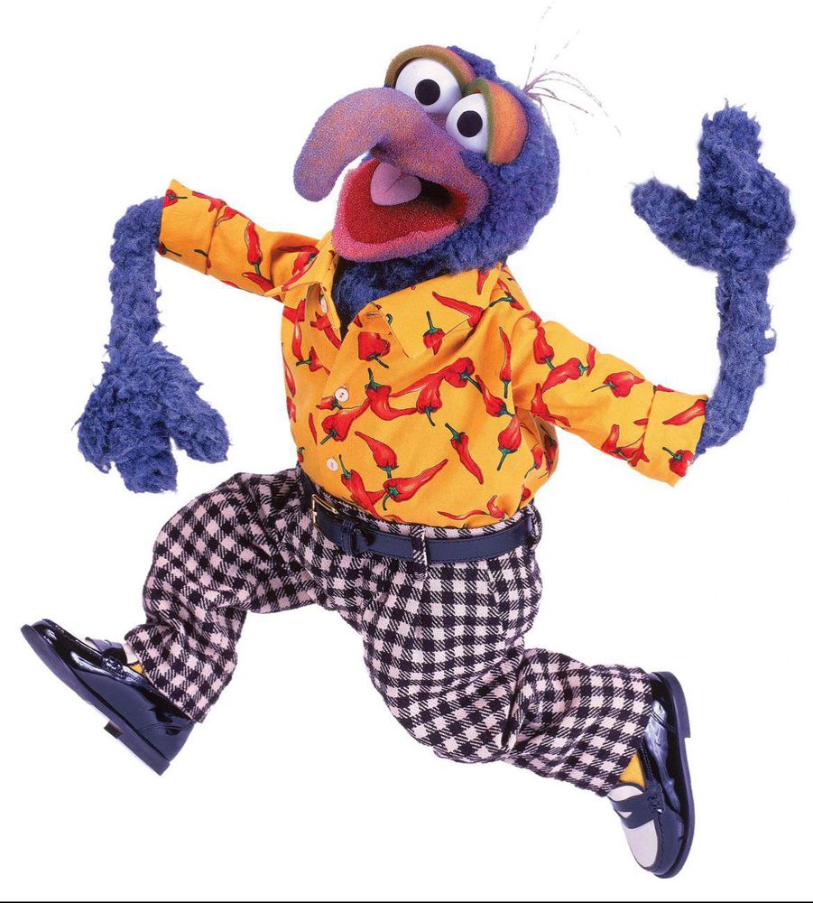 Gonzo from the muppets posed in a silly jump. Gonzo is wearing a yellow button up with red peppers on it, black and white plaid slacks with a blue belt, yellow socks and black and white loafers 