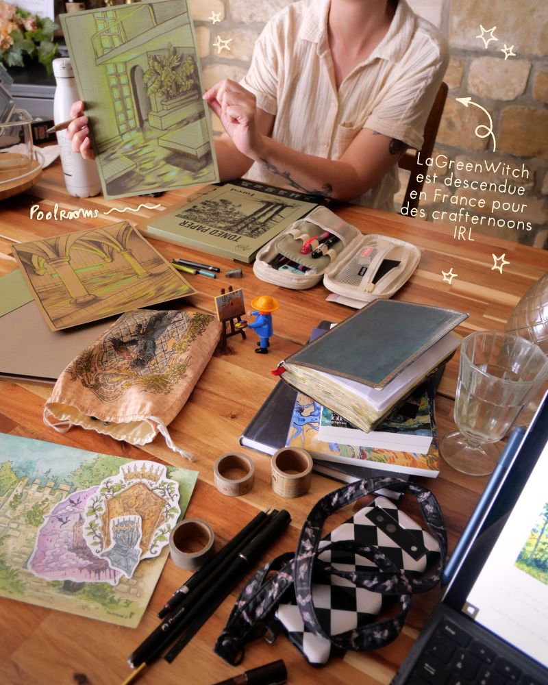 Picture of art atelier with big messy desk. Lagreenwitch is showing her drawing of a green poolroom.