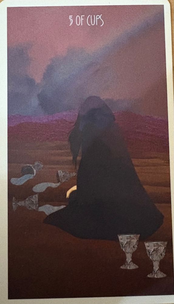 The Five of Cups from the Star Seeker Tarot deck. It shows a hooded, cloaked figure kneeling on the ground, facing 3 spilled cups, their streams being gulped by the earth. Behind the figure, cloaked in black, there are two upright cups, untouched by the tragedy that befell the other three.