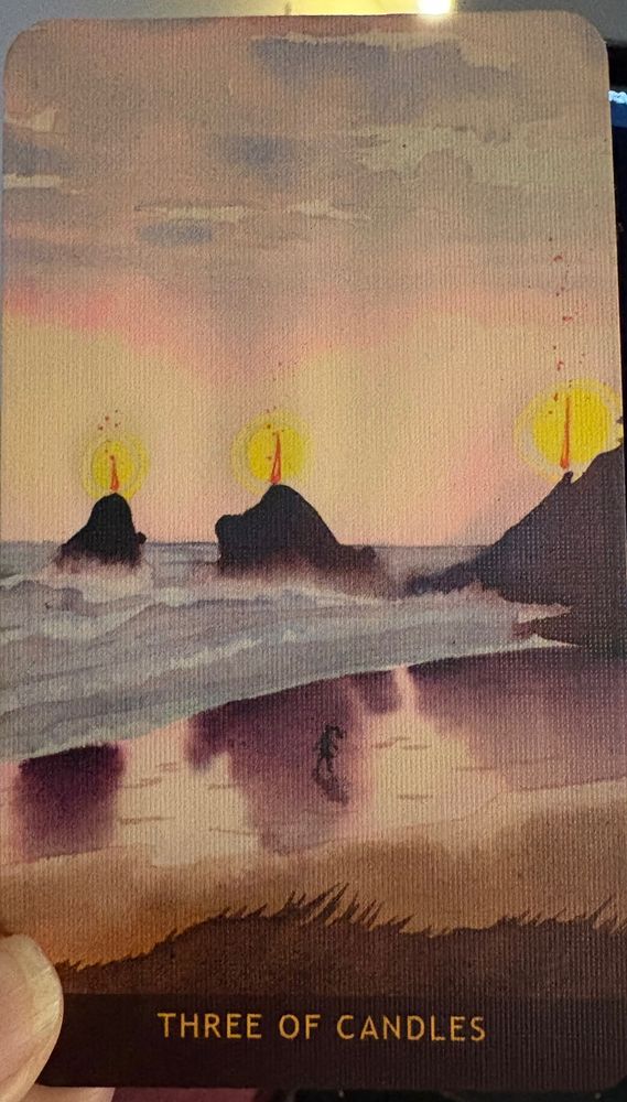 The Three of Candles from the Numinous Tarot deck. From the vantage point of a hill facing a beach, there are three outcroppings of rock sticking out of the ocean that is rolling inland in small but eager waves. On each outcropping there is a red candle glowing with yellow light.