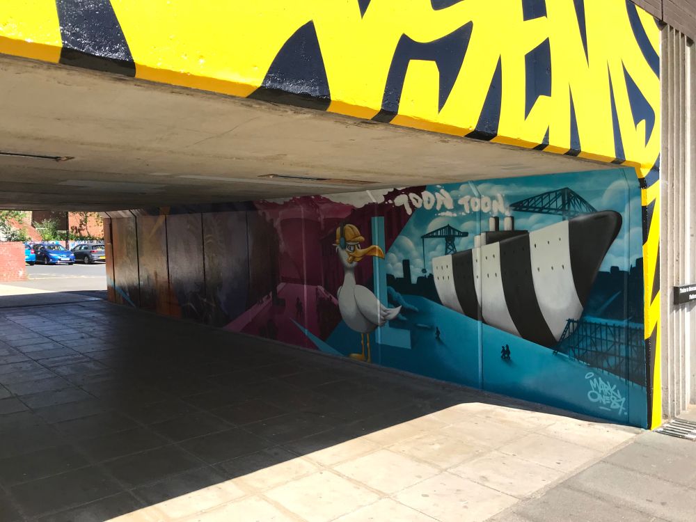View of the mural along the eastern wall of the subway underneath Wallsend Metro station, from the southern entrance. The colourful painting features a Roman soldier, John O'Rourke's statue 