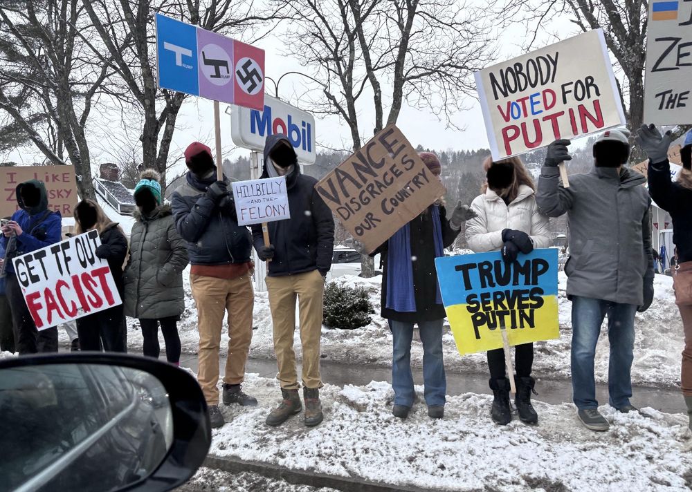 More non-skiers standing on a snowbank with signs saying “Get TF out fascist,” “Hillbilly and the Felony,” “Vance disgraces our country,” “Trump serves Putin,” and “No one voted for Putin” (I would argue a vote for Trump was always a vote for Putin)