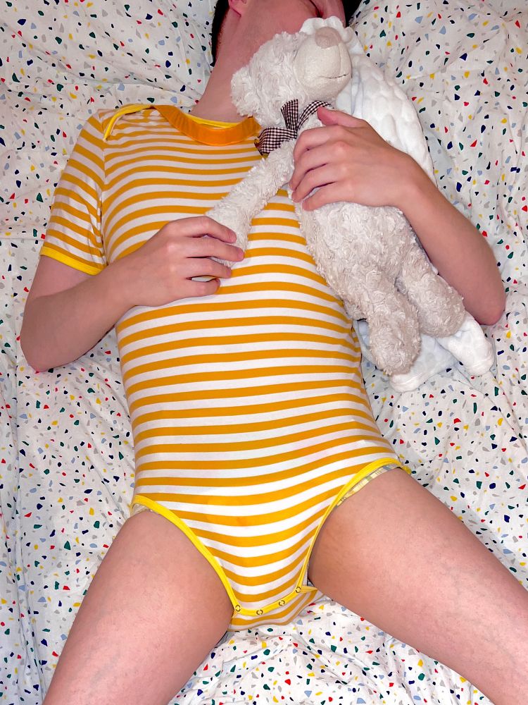 Me in bed in my yellow and white striped onesie and soggy Animooz nappy, with my orange dummy strap around my neck, sleeping and holding Teddy and my blanket