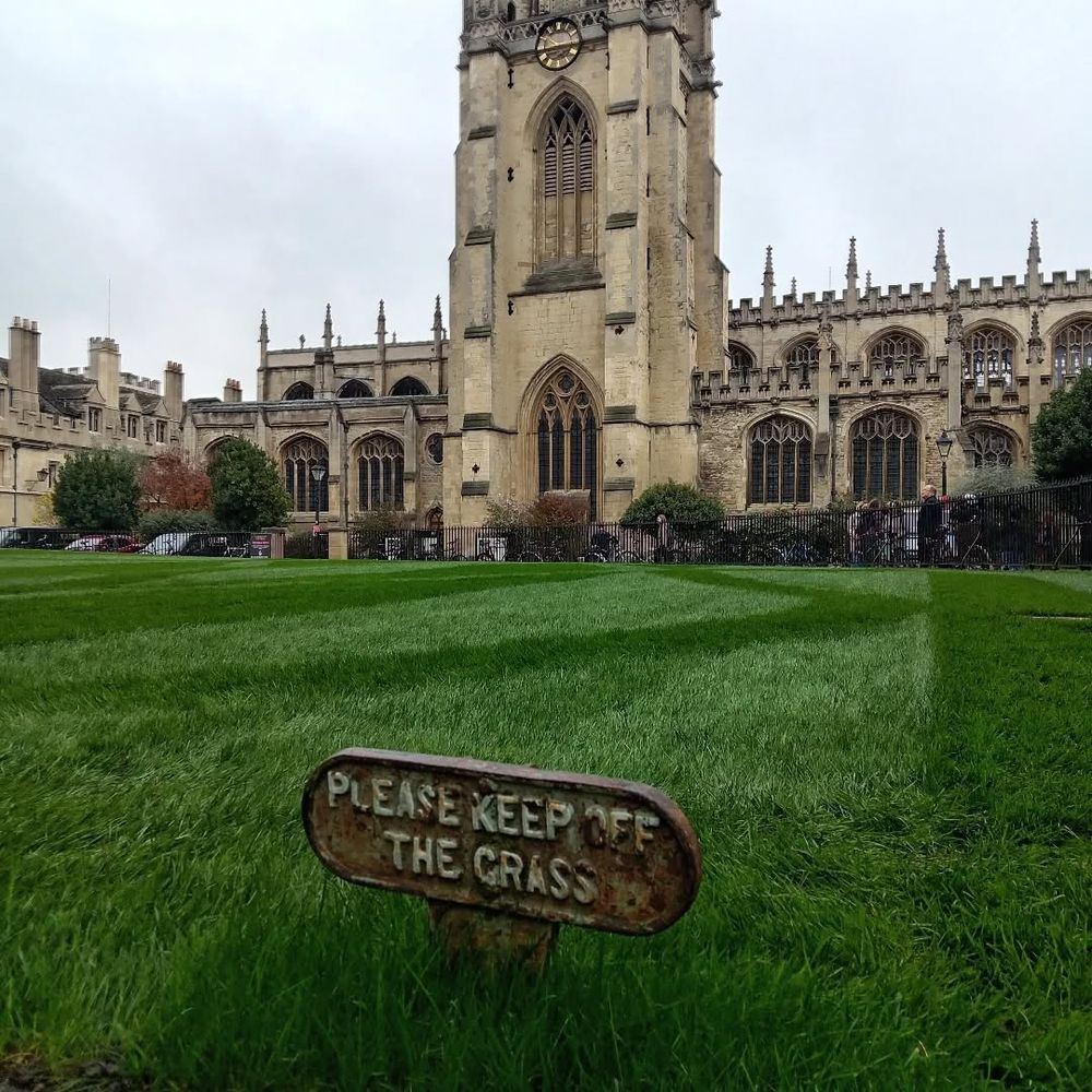 View of a weathered 'Please Keep Off the Grass' sign in the foreground with St Mary's Church in the background.