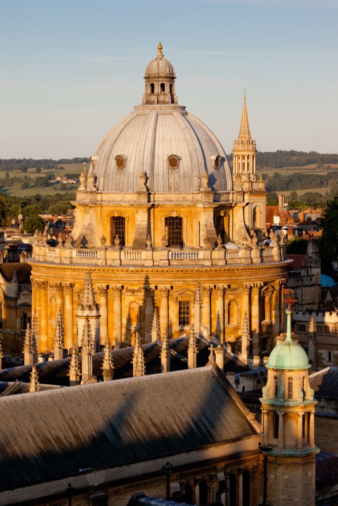 Aerial photograph of the Radcliffe Camera and other rooftops and spires (including the spire of University Church) in the golden light of an early summer morning by Whitaker Studios. 