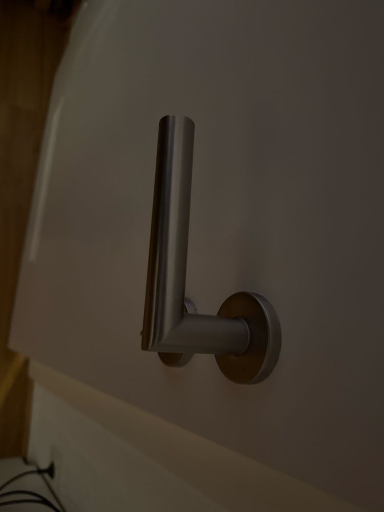 Ein Türgriff in Silber an einer weißen Tür, anstelle das er abgerundet ist, hat er eine spitze 