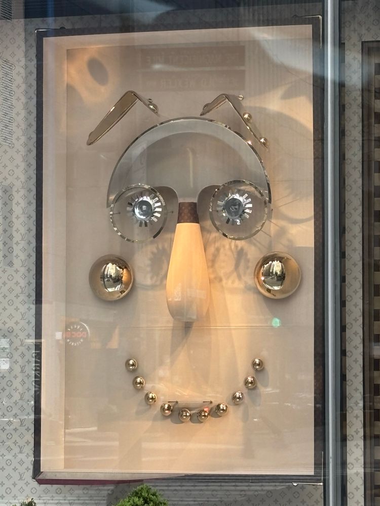 Louis Vuitton store window display, mostly metallic balls making a clown face 