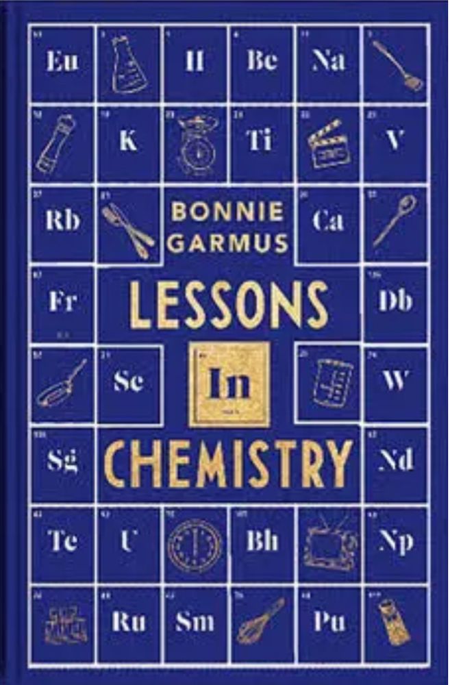 A cover of the book Lessons in Chemistry by Bonnie Garmus. This is a special edition in blue with the periodic table in the background and the book title and author’s name in embossed gold 