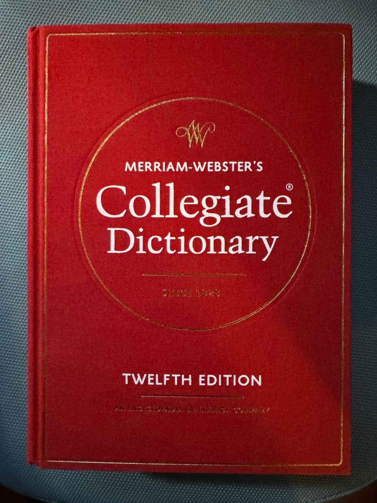 A hard copy of Merriam-Webster's Collegiate Dictionary, 12th Edition, bound with a red cloth cover with white print and gold accents.