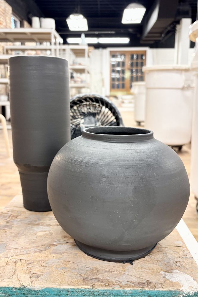 A tall cup with a narrow base to fit 30oz into your cup holder I guess, but even larger and made of black clay still wet off the wheel - and next to it a sphere vase maybe 3 times as wide and half the height, not a perfect round, but not bad either, with just a bit of a rim at the opening. 