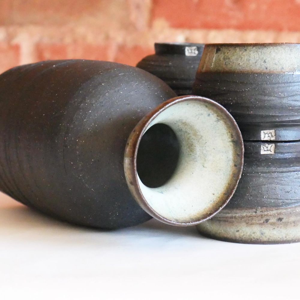 The bottle on its side, opening out to show us the glazed inner lip. we're closer to the cups as well, stacked foot-to-foot, with my m stamp glazed white in relief - and aligned to create a sense of mirroring