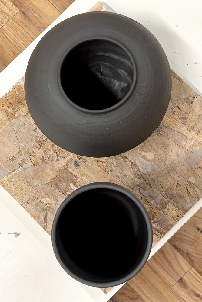 from above, a dark circle the hole of the cup, then concentric shadow on black clay circles for the sphere opening from above. Just circles stacked on a wooden board. 
