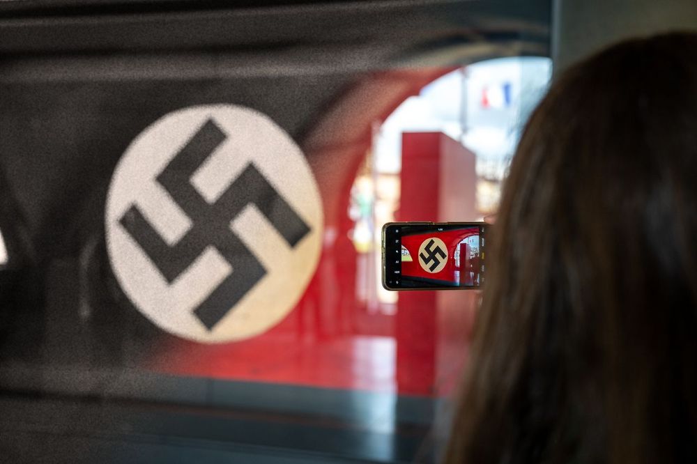1. Un personne prend en photo un drapeau nazi avec son téléphone portable. (Dégradé NB vers couleur, le drapeau nazi est en NB alors que le touriste est en couleur)