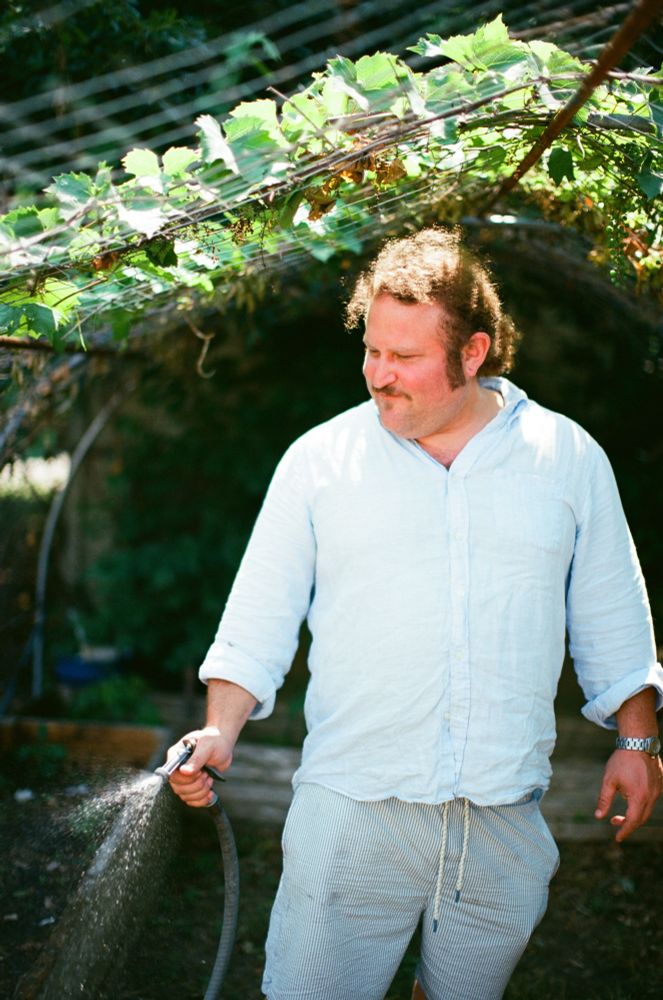 A middle aged man hosing a garden.