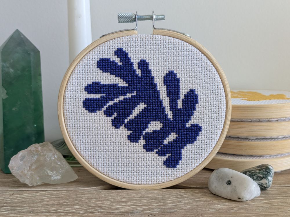 A completed 4-inch cross stitch of a blue plant motif inspired by Henri Matisse