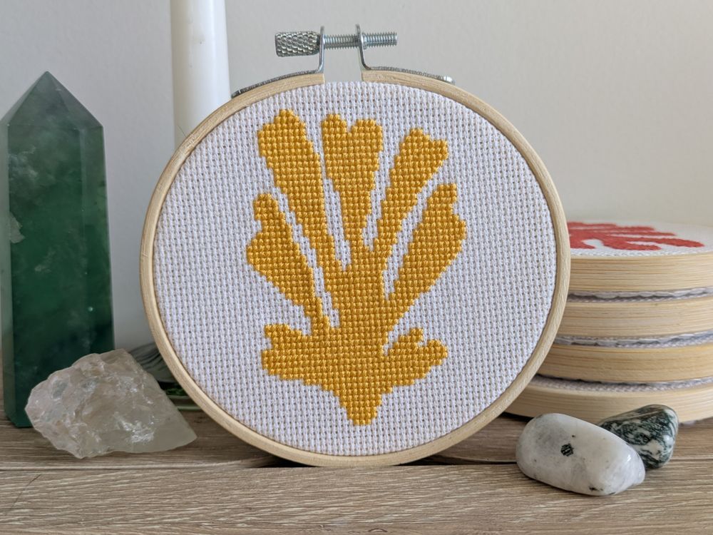 A completed 4-inch cross stitch of a yellow plant motif inspired by Henri Matisse