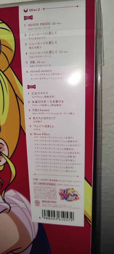 A close-up photo of a Sailor Moon 30th Anniversary vinyl record leaning against a wall. A white tracklist label in Japanese is visible on the top-right corner of the packaging.