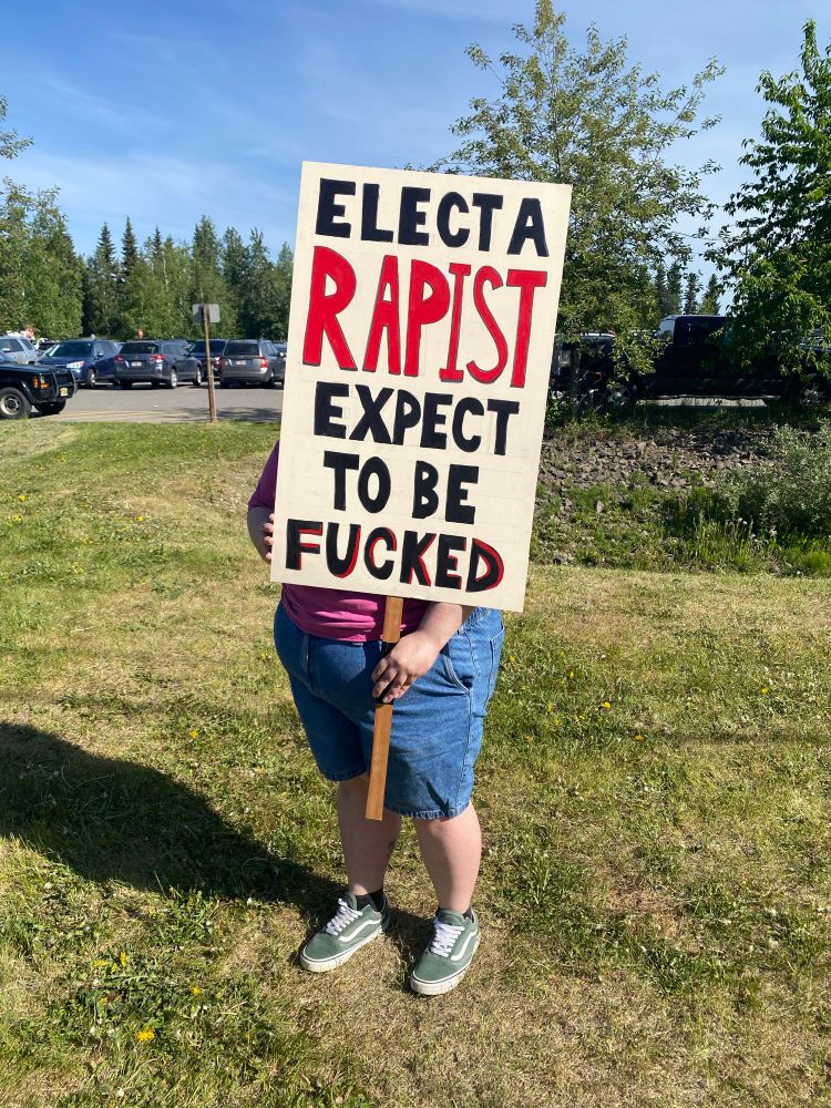 A #NoKings protestor holds a sign that says, Elect a rapist…expect to be fucked. 