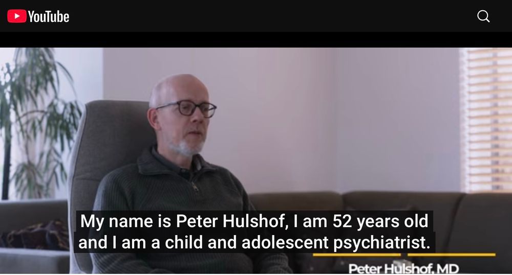 Screenshot of Peter Hulsof from the short film. 
He is sitting in a grey chair with a large plant behind him. 