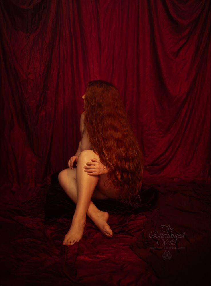 Person with long red hair sitting on the ground with a fully red cloth backdrop