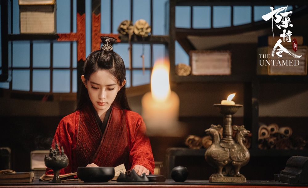 Closeup of Wen Qing (actress Meng Ziyi) in red robes sitting behind a desk, reading. 