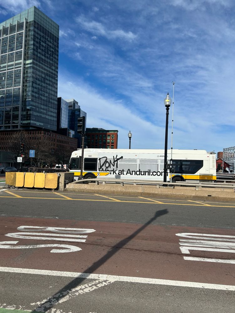 An MBTA bus has the word “Don’t” spray painted over a “Work at Anduril” bus ad. 