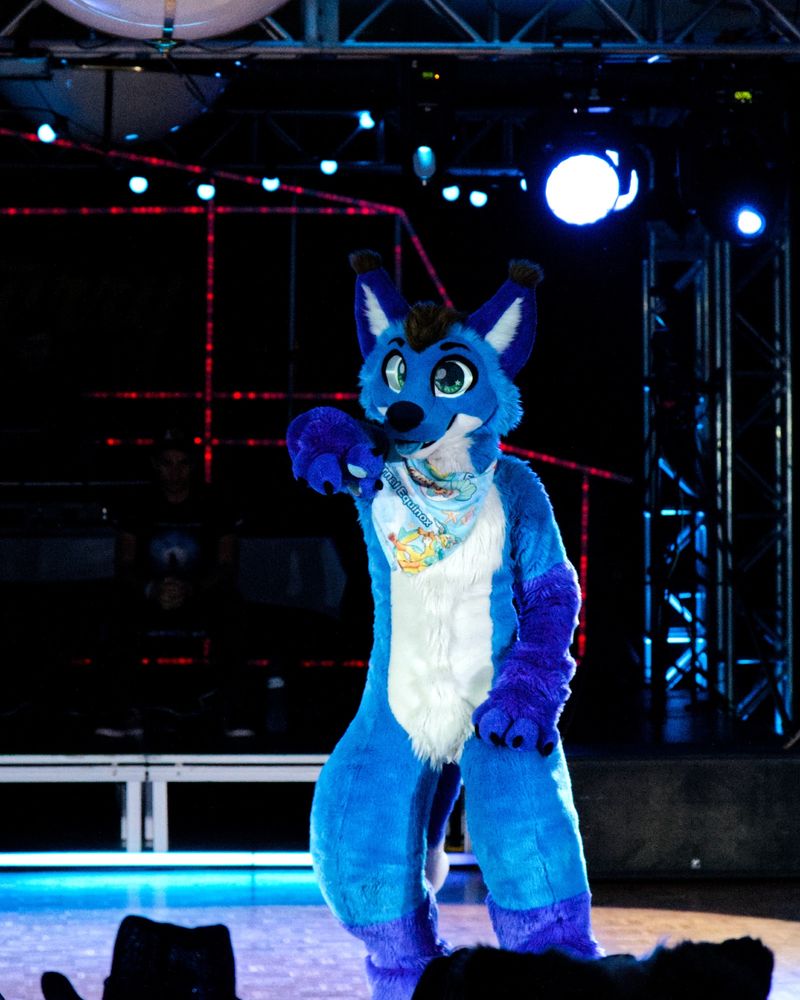 Blue fox fursuiter pointing at the audience in the middle of a dance routine