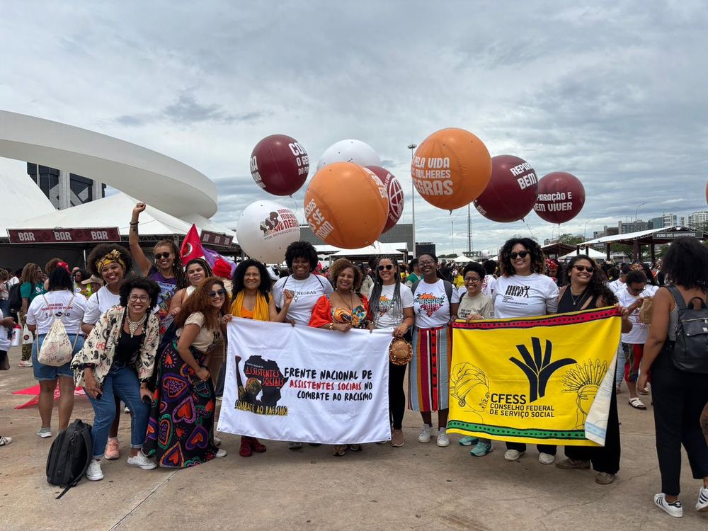 Mulheres, todas negras, seguram bandeiras e cartazes. Atrás há bolas de protestos
