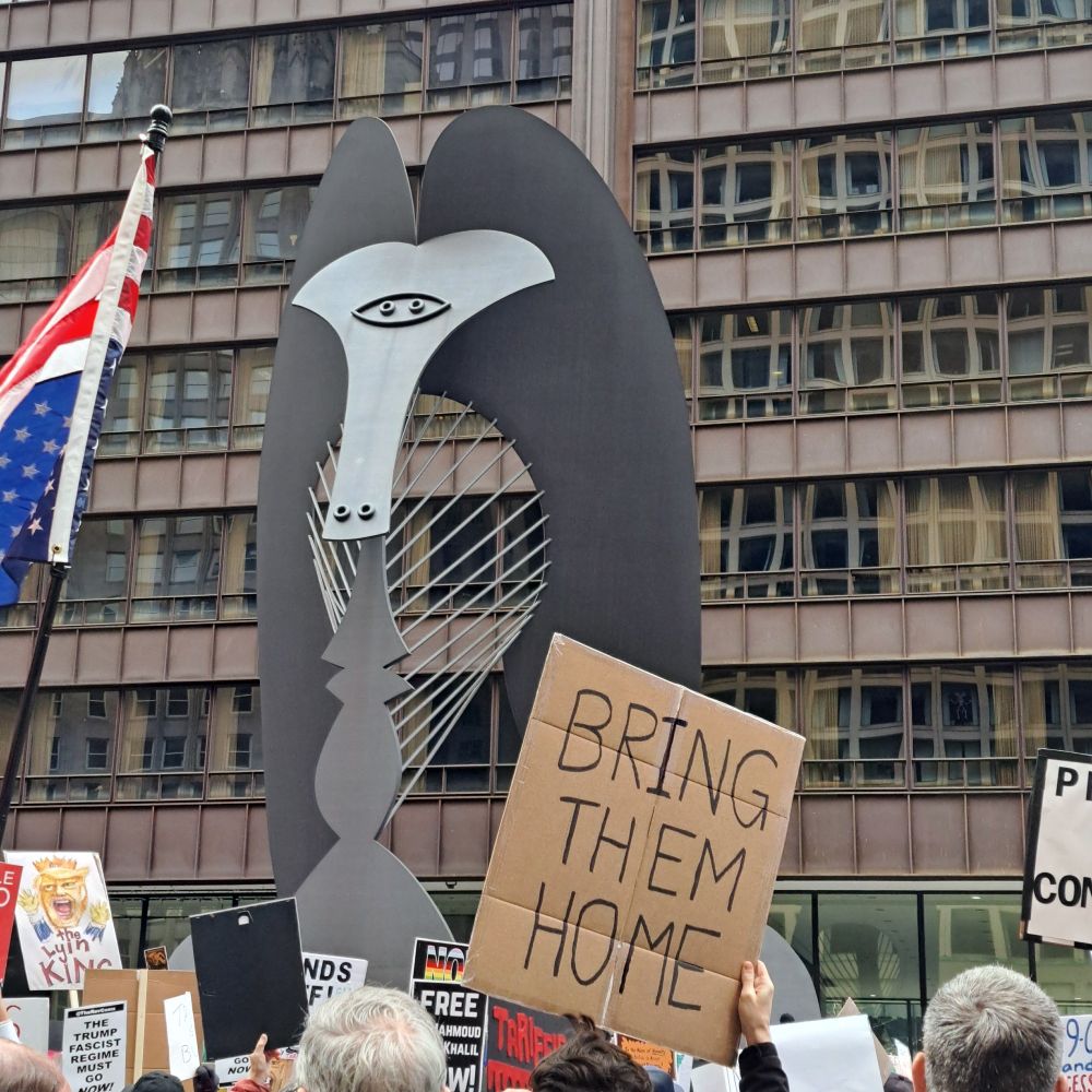 Photo from the back of a protest in Daley Plaza showing a sign that reads, "BRING THEM HOME"