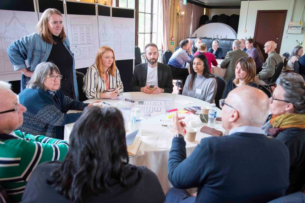 A group of people sit around a table, they are all involved in a discussion and look engaged.
