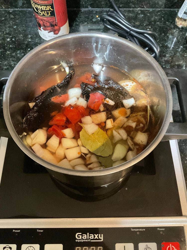 Olla con chiles ancho y guajillo, cebolla y jitomates picadas, hojas de laurel, y especias en agua, sobre un aparato de cocción recién prendido 