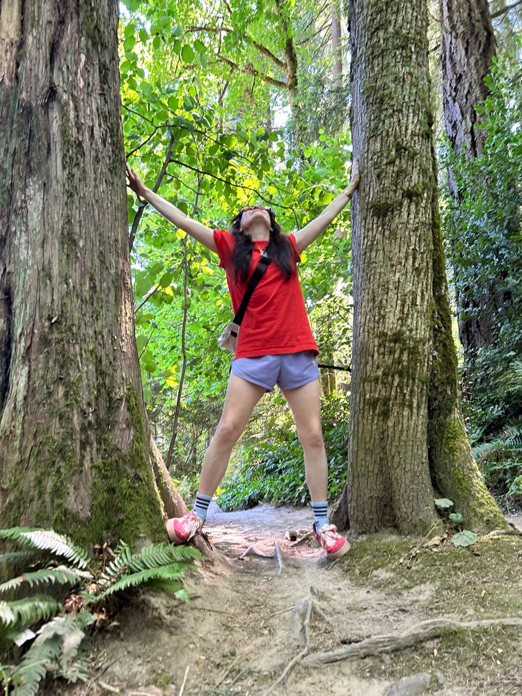 Kay posing between two large pine trees