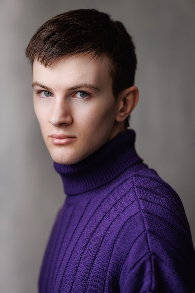 Max with a serious expression, wearing a purple knitted jumper.