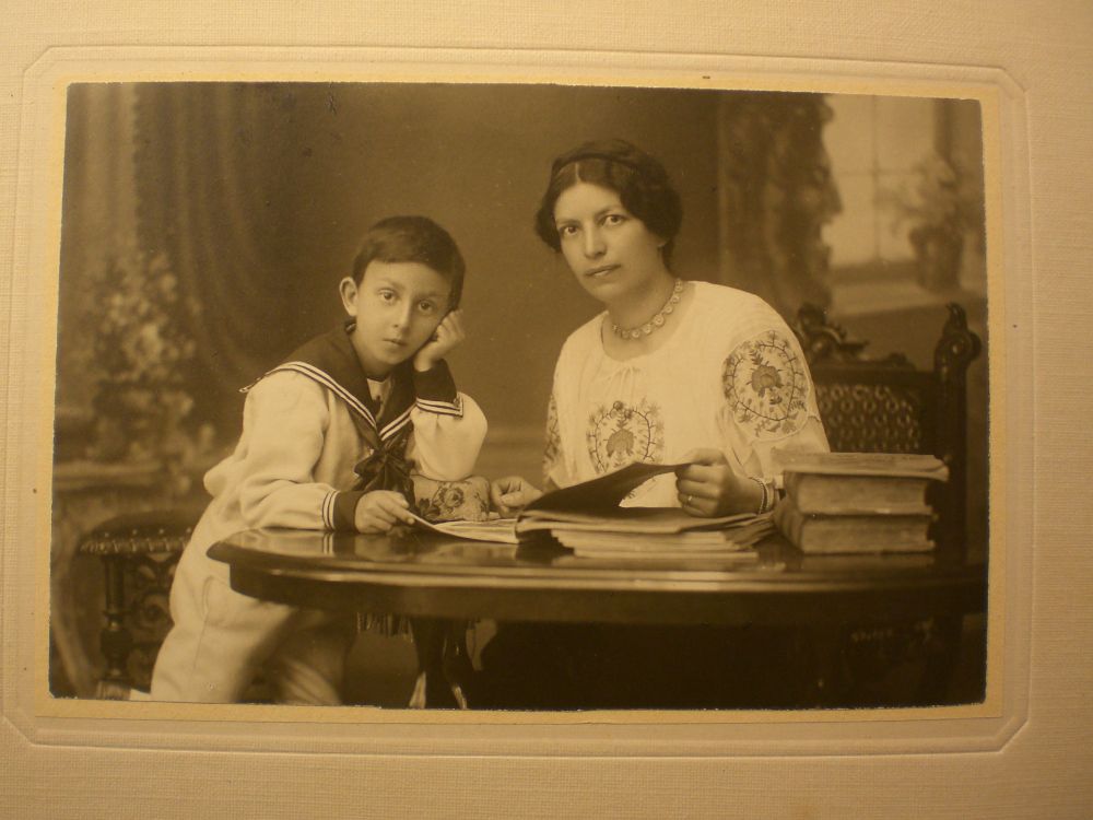Portrait d'une femme et d'un enfant en costume de matelot, extrait des fonds de la famille de James Guillaume aux Archives de l'État de Neuchâtel. Les deux personnes regardent l'objectif alors que sur la table sont disposés des livres. 