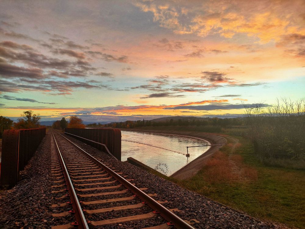 Des rails de train avec en arrière plan un canal et un coucher de soleil épique 