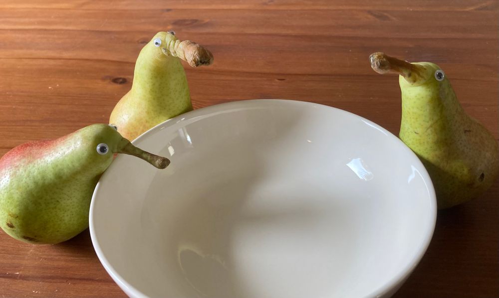 drei birnen mit wackelaugen haben sich um einen leeren suppenteller versammelt und schauen hinein  