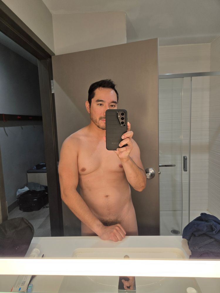 Nude dork taking a bathroom selfie.