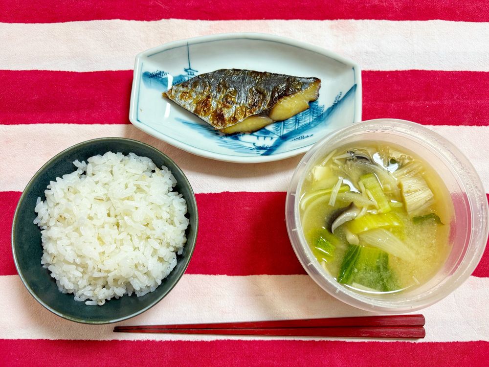 晩ごはんの様子。左下から時計回りに、ご飯、さわらの味噌漬け焼いたん、青梗菜と榎茸と豆腐と平茸の味噌汁。味噌汁はジップロックのスクリューロックに入ったまま食卓に並んでいる。