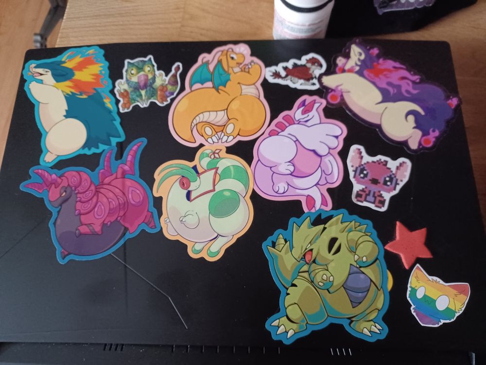 A laptop on a table, showing off the stickers on it.
From top to bottom, left to right : Typhlosion, Pukei-Pukei, Dragonite, Rathalos, Hisuian Typhlosion, Scolipede, Flygon, Lugia (shiny), Angel, Tyranitar, a red Star, a generic furry sporting a rainbow pattern.