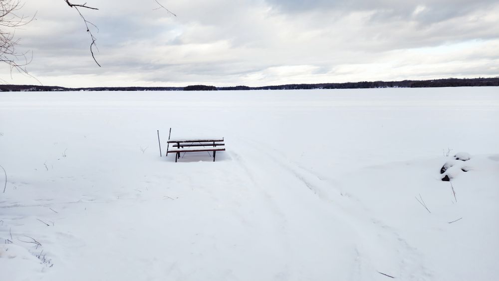 Picnic table on frozen lake with hockey sticks in the snow
